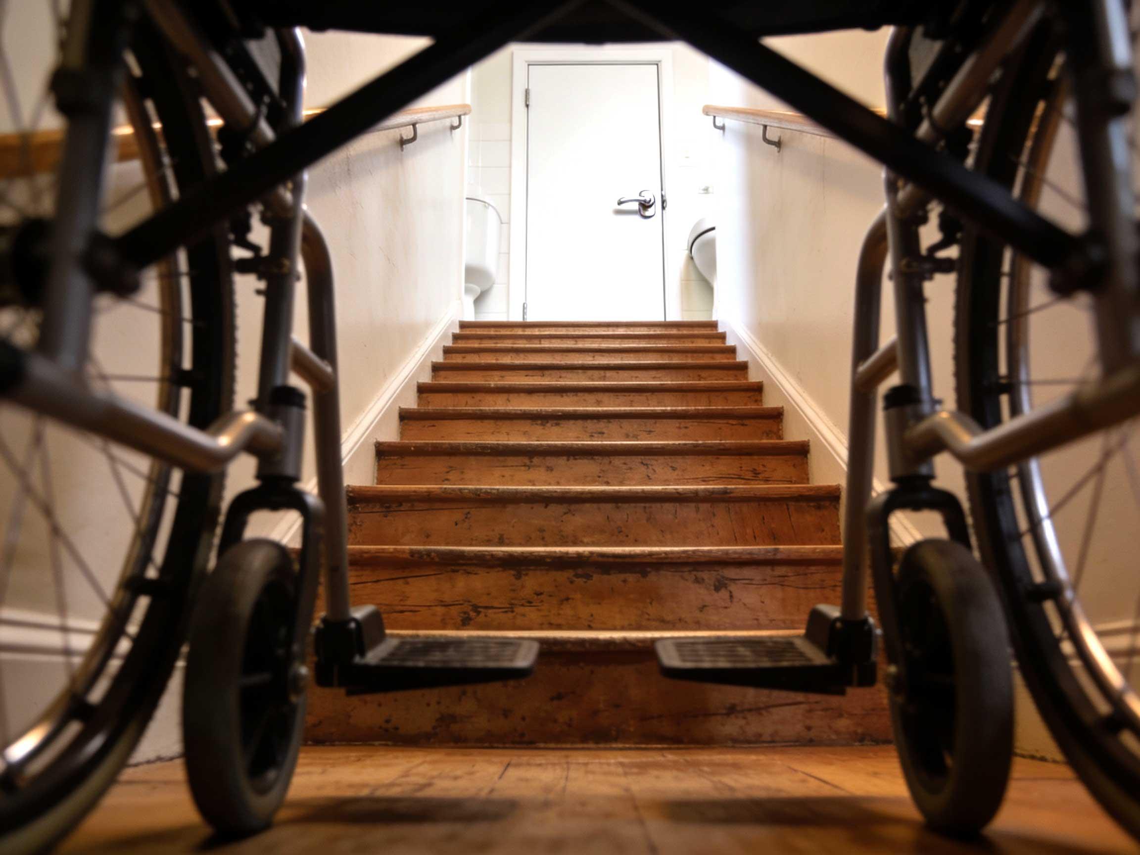View from a wheelchair facing a flight of indoor wooden stairs leading up to a doorway.